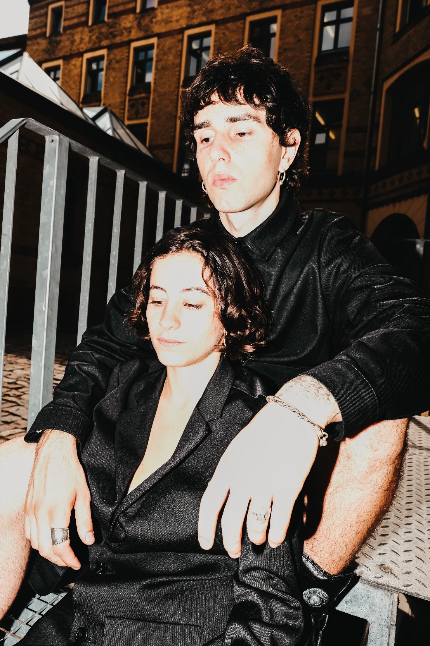 Two people in black outfits sitting close together outdoors.