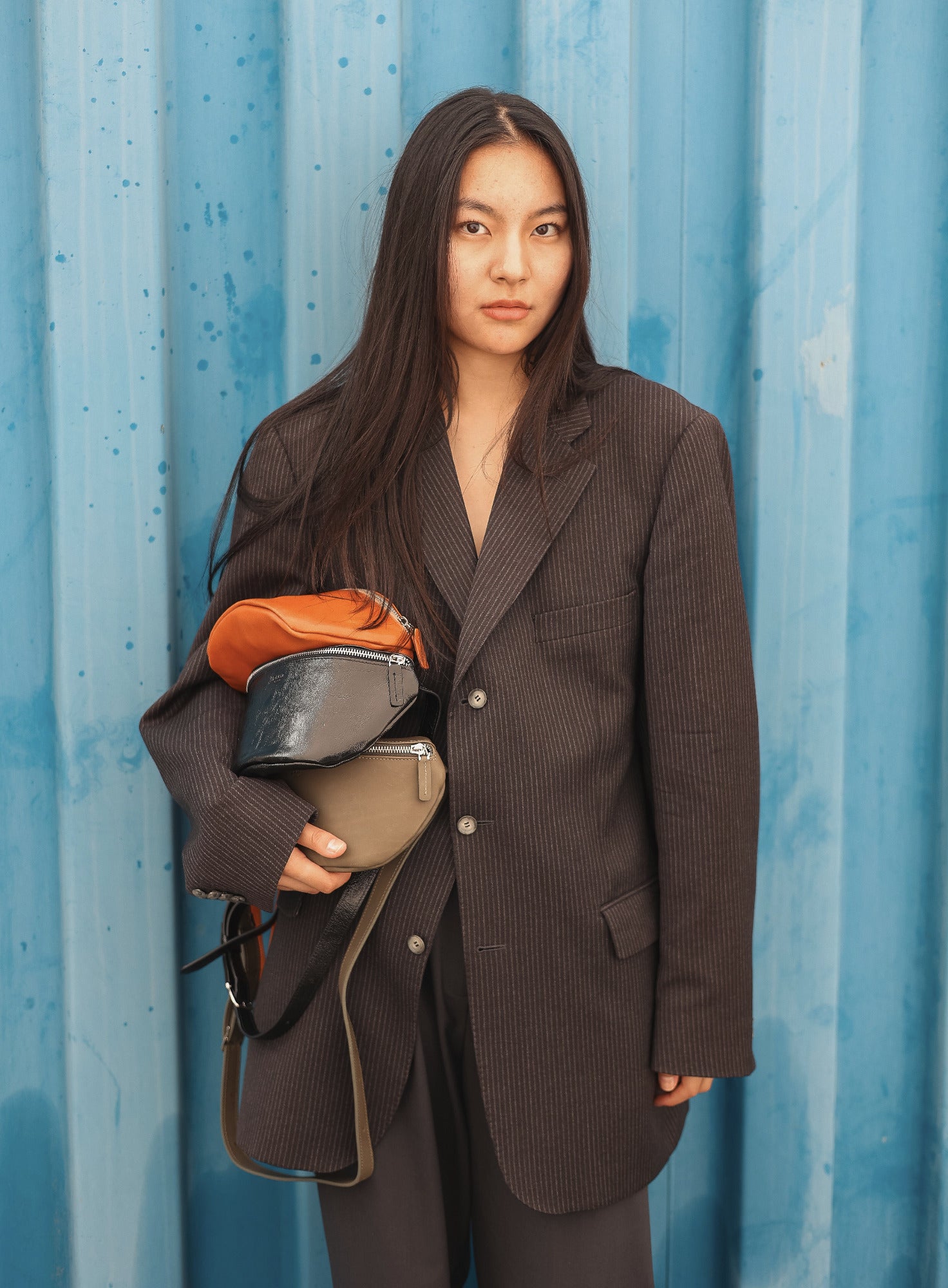 Person wearing a brown suit holding multiple bags against a blue corrugated metal background
